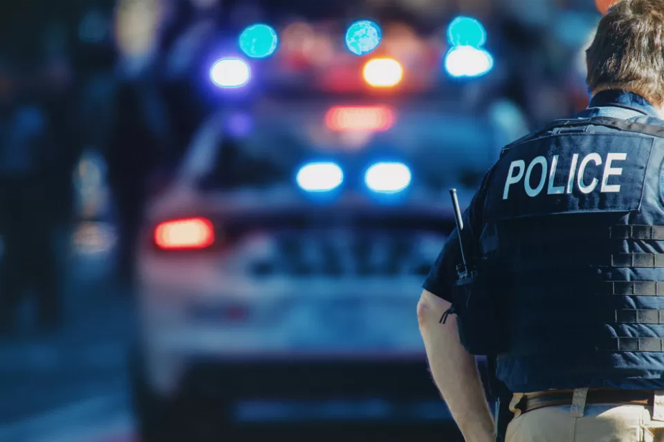 Police officer with POLICE on the back of their vest with police car in the background
